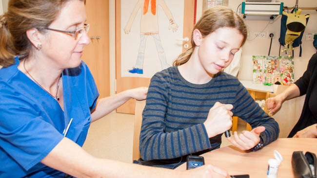 Die Kinderdiabetologin Dr. Marina Sindichakis macht den 12-Jährigen Damian mit dem regelmäßigen Blutzuckermessen sowie der Insulinpumpe vertraut  