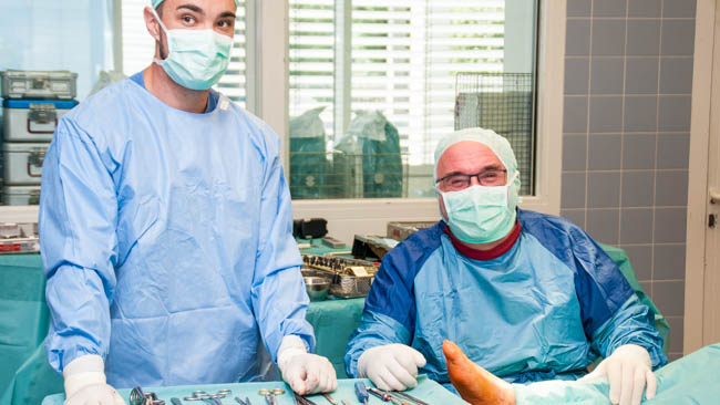 „Wir sind ein eingespieltes Team und operieren immer mit derselben Mannschaft“, Dr. Alfred Leitner (rechts sitzend) – Die Operation kann los gehen. Unterstützt wird er im Bild von Volker Schachner (li.), Operationstechnischer Assistent.